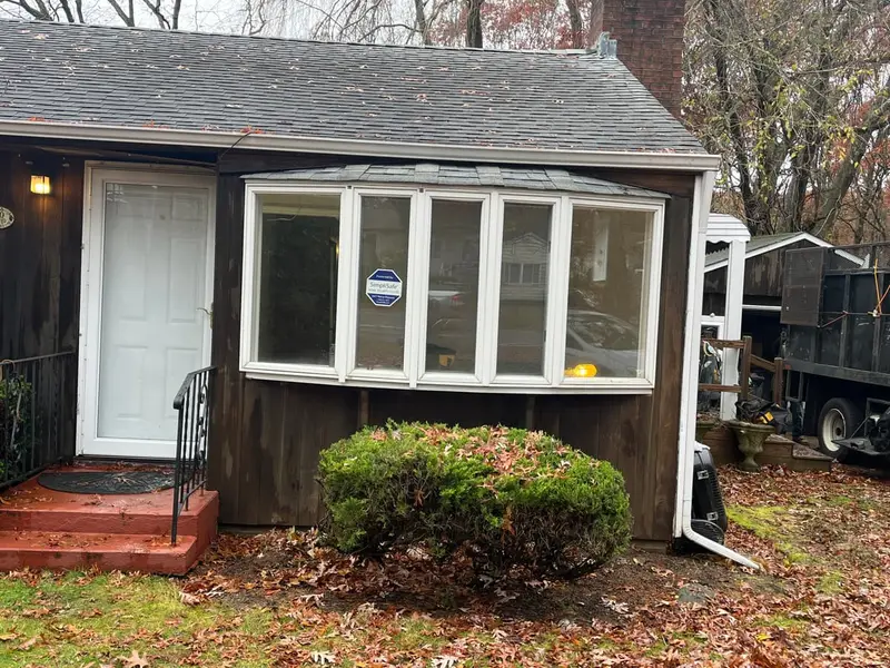 Small dark-shingled cottage with a bay window and a brick stoop, Ronkonkoma, NY